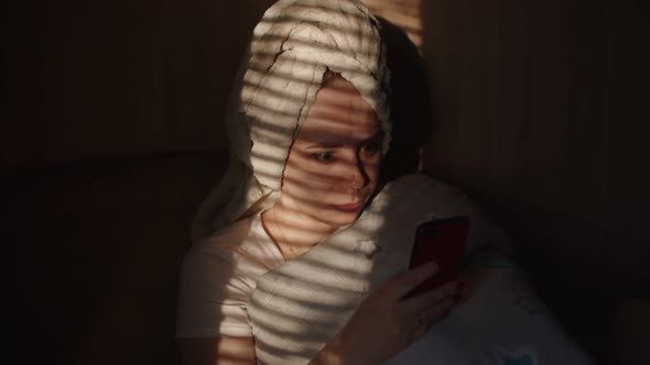 Close Up of Young Woman with Towel on Her Head Browsing Smartphone in Dark Room alt