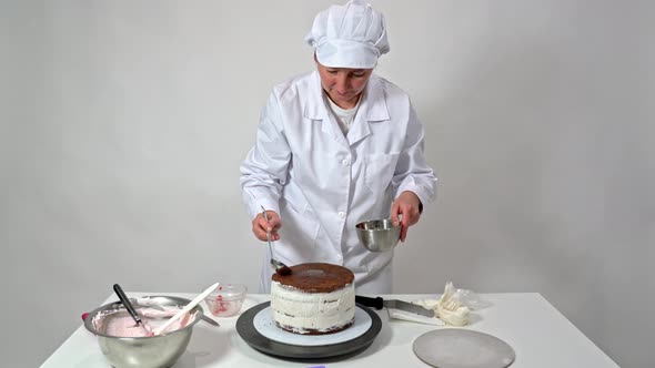 A Middleaged Woman Baker Pours Syrup on a Wedding Cake with Chocolate Brownies