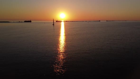 Beautiful aerial vibrant high contrast sunset over calm Baltic sea, distant sailing boat, rock pier alt