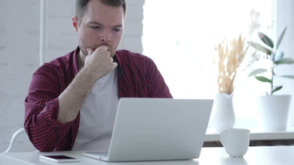Pensive Young Man Thinking and Working on Laptop alt