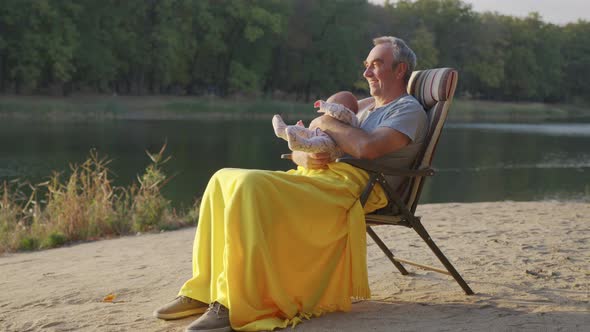 Grandfather Holding Newborn Baby Granddaughter Outdoors. alt