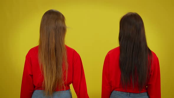 Back View Two Slim Young Beautiful Women at Yellow Background Holding Hands alt