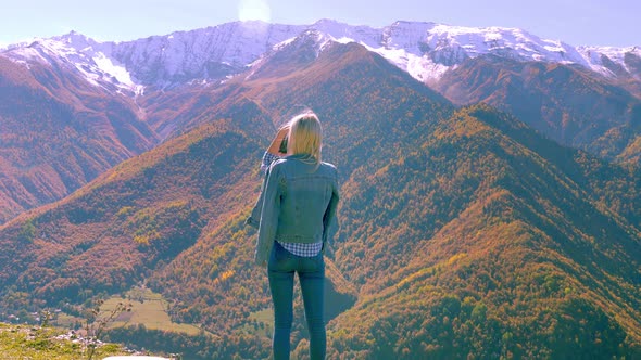 beautiful blonde takes photos or videos of a landscape in the autumn mountains. alt