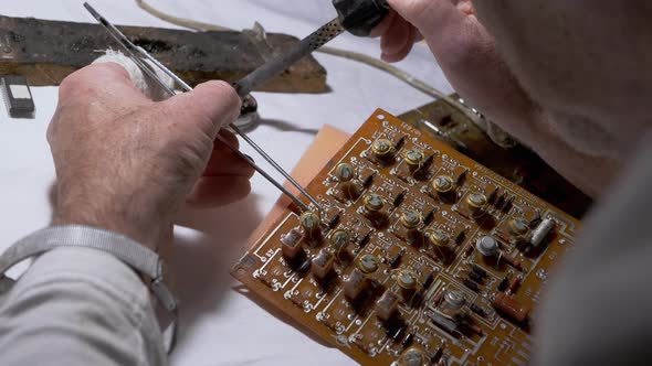 Man Solders Transistors Radio Parts on Electronic Board with Soldering Iron alt