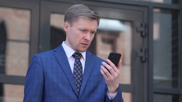 Wondering Businessman in Shock while using Smartphone alt