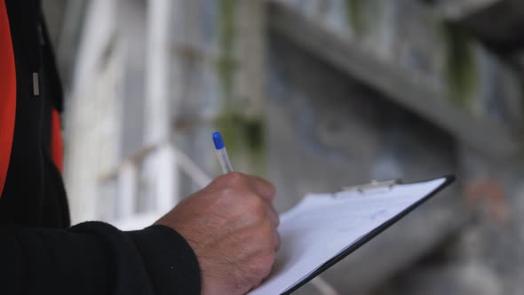 Closeup of a Male Engineer Making Entries in a Technical Log While Inspecting a Construction Site or