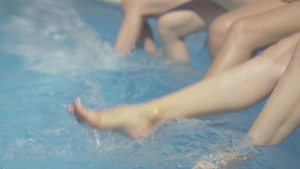 Slim Female Caucasian Feet Splashing Water in Swimming Pool at Resort. Unrecognizable Young Women alt