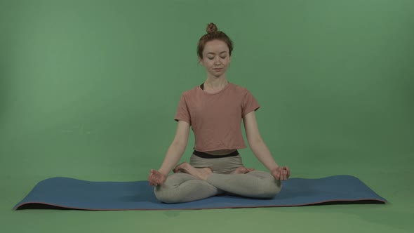 A Young Beautiful Athletic Girl Sits in a Lotus Position Against the Chroma Key alt