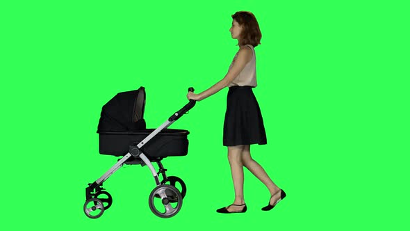 A mother walking with a stroller, looking around and at her baby, smiling, over a green screen. 4K alt