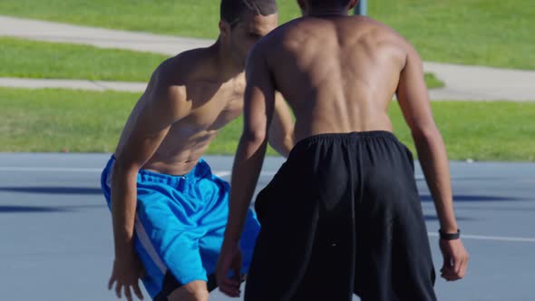 Friends playing basketball at park, one on one