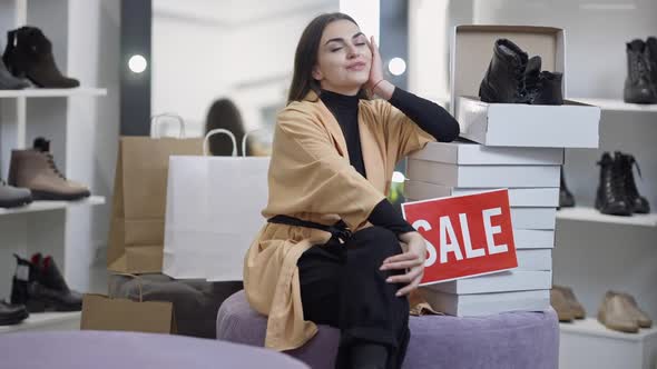 Wide Shot Satisfied Female Client Sitting in Shoe Shop with Lot of Boxes Smiling alt