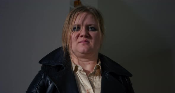 Battered Young Woman with Smeared Makeup on a Serious Angry Face Wearing Leather Coat Aims a Gun at