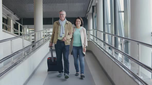 Senior Couple Walking with Luggage in Airport Walkway. Aged Travelers Going To Board Plane alt