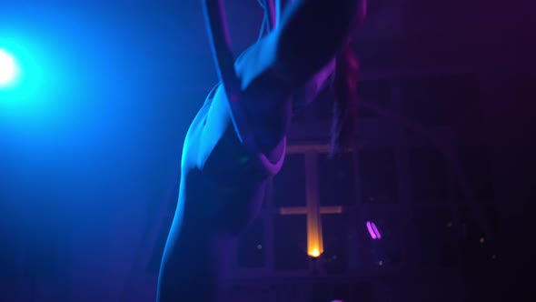 Silhouette Aerial Gymnast Performs Trick in Ring in Smoky Room with Backlit alt