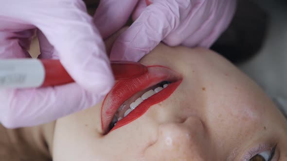 Closeup of a Permanent Makeup Master with a Red Pen Draws a Contour Sketch of Future Lips