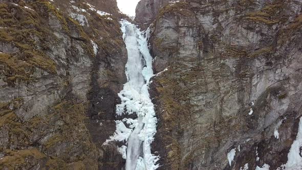 Aerial View of an Icy Waterfall Cutting Through a Cliff in Norway, Slow Decending Motion alt