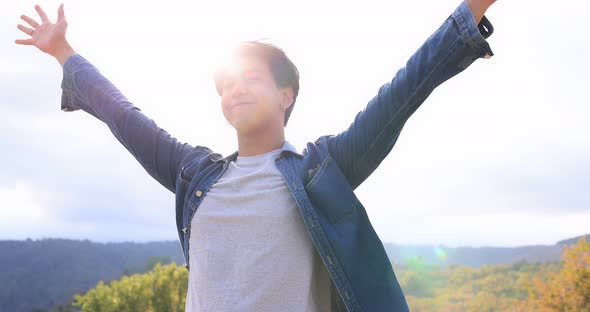 Freedom Asian young man raising hands on the top at the mountain. alt