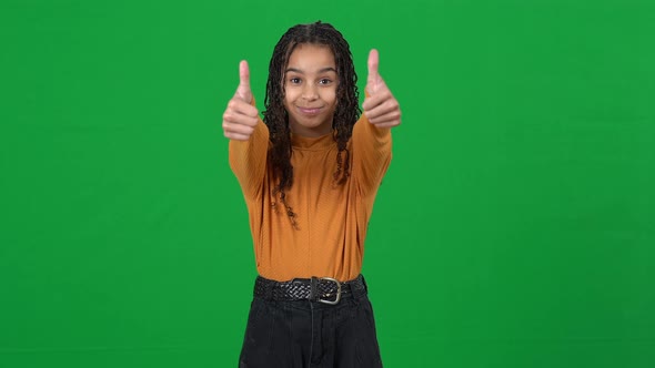 Portrait of Positive Joyful Teen African American Girl Showing Thumbs Up Looking at Camera on Green alt