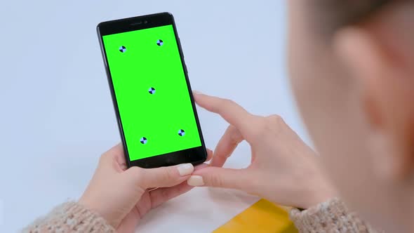 Woman Looking at Black Smartphone Device with Empty Green Screen