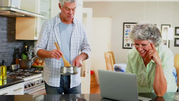 Senior couple using laptop while cooking in kitchen 4k alt