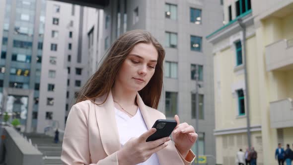 Portrait of Confident Business Woman Typing By Mobile Phone While Walking Outdoors at City Street alt