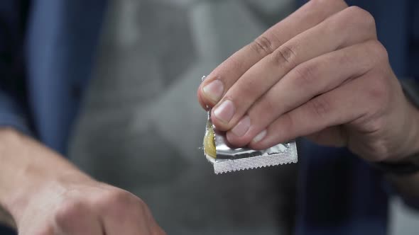 Male Hand Opening Condom Package Before Camera, Contraception, Close-Up alt