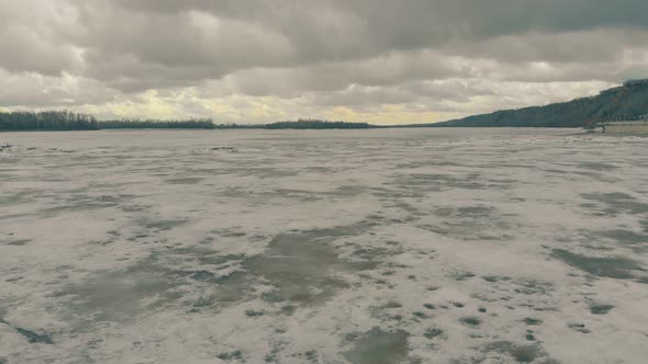 Heavy Grey Clouds Above Dirty Brown Frozen River Surface alt