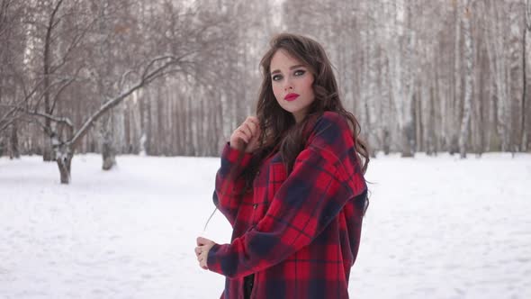 Young Woman with Wavy Hair Standing and Touching Face in Winter Forest