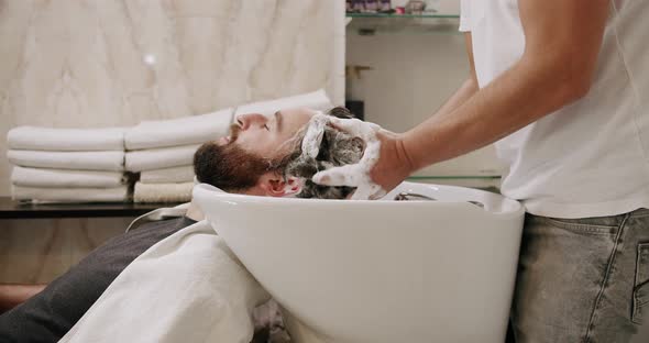 The Man in the Beauty Salon is Served Washing His Head with Shampoo and Water alt