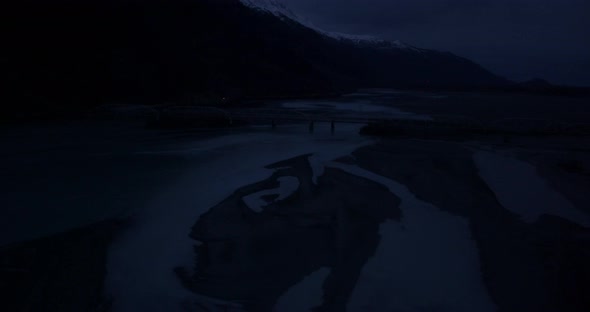 Aerial helicopter shot, flyover frozen river past glacier, large icebergs, mountains in background, 