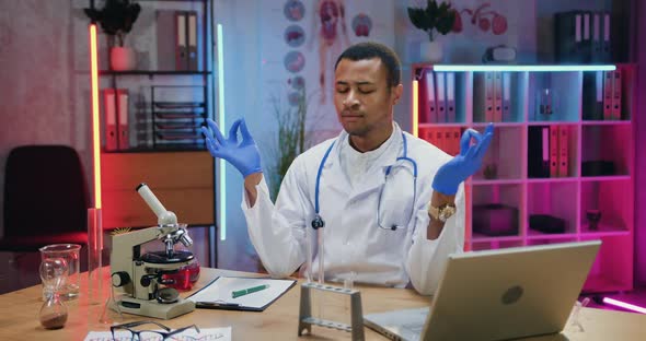African American Male Chemist in Uniform Meditating with Closed Eyes in Evening Lab alt