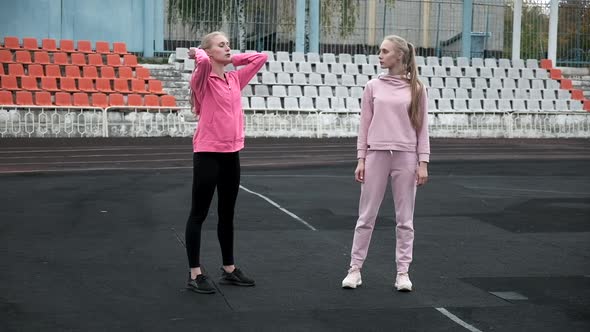 Caucasian Identical Pretty Twins in Sportswear Do Squats Exercise at Stadium