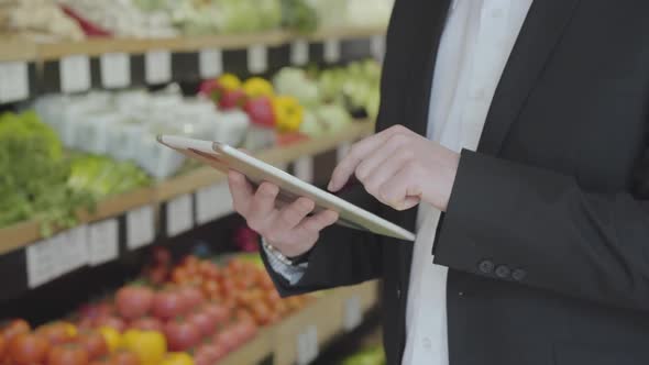 Close-up of Male Caucasian Hands Using Tablet in Grocery Store. Unrecognizable Adult Man in Suit alt