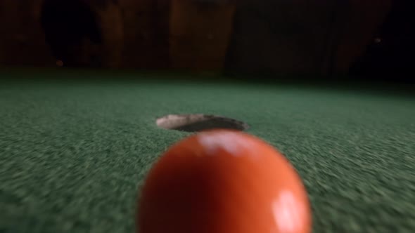 An orange mini golf ball slowly falls into the golf hole and bounces in the pocket on a course. alt