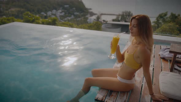 A Blonde Woman Drinks Mango Shake While Lounging in the Sun By the Pool on Vacation alt