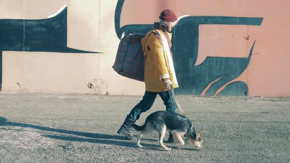 A Homeless Man is Leading a Dog Along the City Street alt