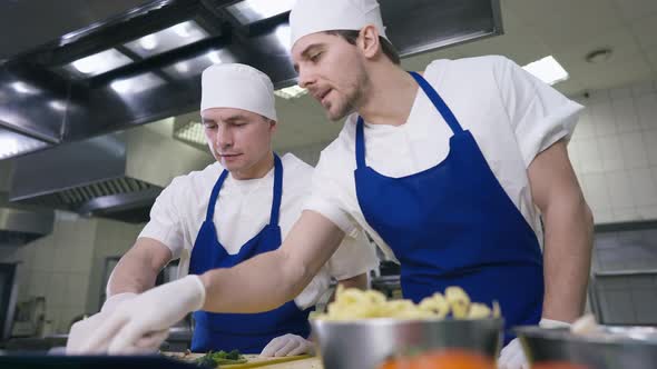 Portrait of Confident Professional Young Chef Talking to Unsure Cook Pointing at Order Recipe alt