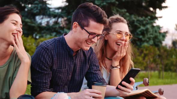 Happy Smiling Teenage Friends Laughing Outside at Something in Smartphone or Mobile Phone alt
