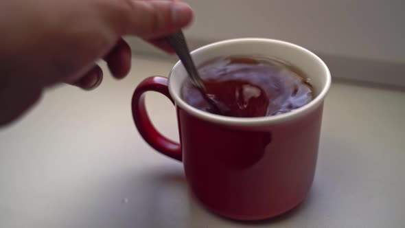 Human's Hand Pours Spoonful of Sugar Into Ceramic Mug with Tea