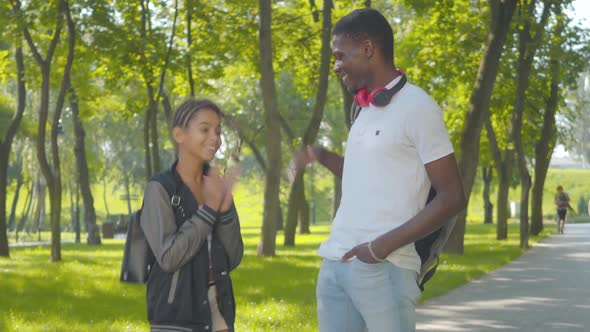 Portrait of Joyful Young Man and Little Girl Standing in Sunny Park and Talking. Happy African alt