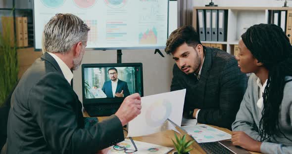 Business Team Explaining Report with Chart to their Bearded Head of Company During Online Video chat alt