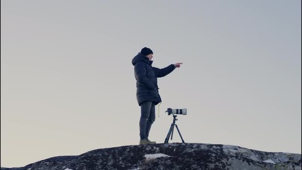 Man Pointing From Top Of Rock With Camera On Tripod alt