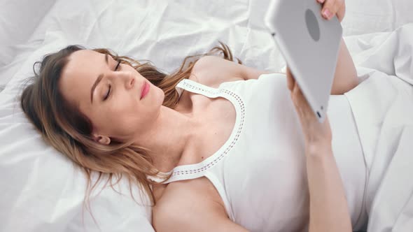Smiling Young Girl Looking at Screen of Tablet Pc Lying on Bed alt