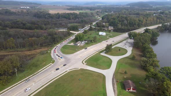 Aerial view of rural highway and county road intersection with car tour. Forest and mountains seen.