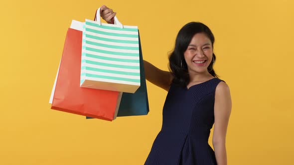 Asian woman waving her hand and showing colourful shopping bags
