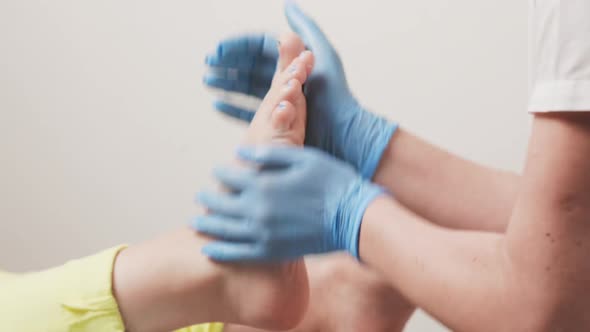 Master chiropodist in blue medical gloves massages a female foot. Closeup of hands and legs alt