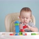 A joyful newborn 12-17 months old builds a tower of wooden cubes sitting on a chair. - VideoHive Item for Sale
