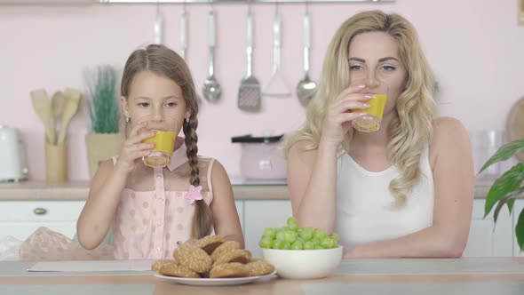 Happy Caucasian Mother and Daughter Drinking Healthful Orange Juice, Talking, and Smiling at Camera alt