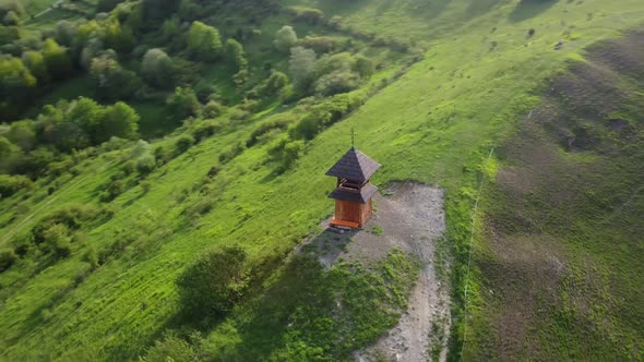 Christian bell tower, a chapel on a green hill in the countryside. Forged cross on the roof.