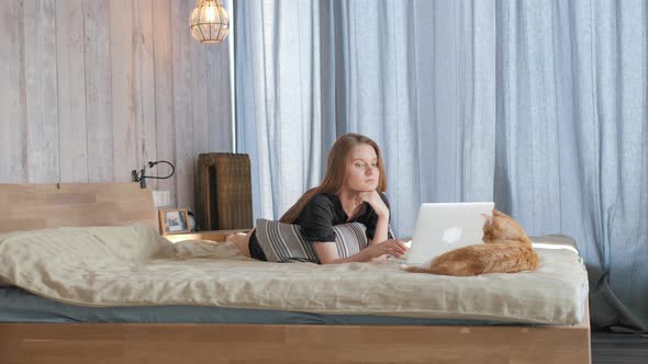 Blonde Pretty Girl with Ginger Cat Surfing Internet on Laptop at Home